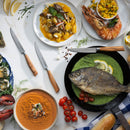 A seafood feast—whole fish with lemon, prawns with salsa, gnocchi, oysters, soup, bread, cherry tomatoes—beautifully presented alongside the Messermeister Oliva Elite Next Level Block Set (11-piece) for an elegant touch.