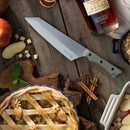 A knife, apple pie, apple slices, cinnamon sticks, brown sugar, and a bottle of bourbon are arranged on a rustic wooden table, with the knife resting beside the Messermeister Overland Chef 6-Piece Leather Knife Roll Set by Messermeister—a perfect storage solution for any outdoor cooking knives.