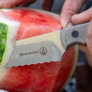 A close-up of a hand using the Messermeister Overland Chef Scalloped Slicer - 8" to cut through a watermelon rind, showcasing the serrated edge by Messermeister.
