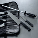 A Messermeister Fine Grit Honing Steel - 12" is displayed on a gray surface with several kitchen knives, some inside a black fabric case and others placed next to it.