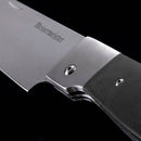 Close-up of a Messermeister Adventure Chef Linen Folding Chef's Knife - 6" with a stainless steel blade and textured black handle, set against a black background.