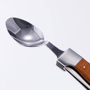 A close-up of the Messermeister Adventure Chef Maple Folding Camp Utensil shows its metal spoon and wooden handle, angled diagonally against a plain white background, highlighting light reflections on its shiny surface.