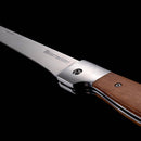 Close-up of the Messermeister Adventure Chef Maple Folding Flexible Fillet Knife - 6" with a wooden handle and German stainless steel blade, partially open against a black background, highlighting its sleek craftsmanship.