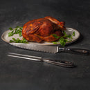 A whole roasted chicken garnished with parsley is served on an oval plate beside a Messermeister Avanta Damascus knife from the 10-piece block set, all displayed on a dark surface.