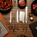 The Messermeister Avanta Forged Pro BBQ Knife Set (6 Piece) by Messermeister, featuring high-carbon stainless steel blades and wooden handles, is arranged on a table with sauces, seasonings, and grilled meats—ideal for grill masters.