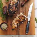 Sliced grilled chicken breast on a wooden cutting board is served with the Messermeister Avanta Steak Knife Set - 4 Piece by Messermeister, alongside a bowl of seasoning and fresh rosemary sprigs.