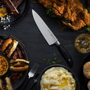 A dark table set with fried chicken, mashed potatoes, mini burgers, corn, whiskey, ribs, a biscuit, baked macaroni—and a Messermeister Blacksmith Next Level Block Set - 5 Piece high-carbon stainless steel knife.