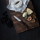 The Messermeister Blacksmith Next Level Block Set - 5 Piece by Messermeister is elegantly displayed on a dark surface, surrounded by a wooden cutting board with blue cheese, soft cheese, sliced figs, and grapes.