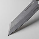 Close-up of the pointed tip and edge of the Messermeister Carbon Bunka Chef's Knife - 8" with a grey blade, featuring the Messermeister logo engraved on its surface, shown against a plain light background.
