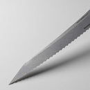 Close-up of the Messermeister Carbon Scalloped Knife - 9" blade resting on a light gray surface, its edge casting a shadow.