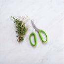 A small bundle of fresh herbs and white flowers rests on a white marble surface beside Messermeister Culinary Scissors - 6", featuring green handles and sharp stainless steel blades.