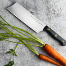 The Messermeister Custom Nakiri Knife - 6.5" features a sleek black handle and Japanese-inspired design, shown on a gray surface beside fresh carrots—ideal for effortless vegetable preparation.