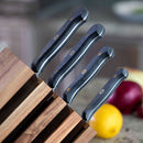 Four Messermeister Custom Next Level knives with black handles are displayed in a wooden Messermeister magnetic knife block set on a kitchen counter, with a lemon and a red onion visible in the blurred background.