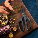 The Messermeister Esther Choi Push Button Take-Apart Precision Shears - 7" rest on a wooden cutting board amid chopped herbs, raw shrimp, multicolored corn, halved cherry tomatoes, and a bowl of vegetable salad on a dark blue background.