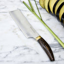 The Messermeister Kawashima Nakiri Knife - 6.5" with a wooden handle rests on marble beside sliced eggplant and lemongrass stalks.