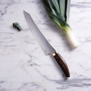 The Messermeister Kawashima Slicer - 10" by Messermeister, featuring a wooden handle and Japanese craftsmanship, rests on a marble surface beside a whole leek and several sliced pieces.