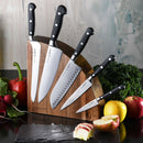 The Messermeister Meridian Elite Magnet Block Set - 6 Piece features German hand-forged knives with black handles in a stylish wooden block, surrounded by fresh vegetables, leafy greens, and apples on a black countertop.