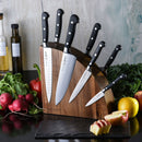 The Messermeister Meridian Elite Magnet Block Set (8 Piece) by Messermeister features black-handled knives in a wooden magnetic block, displayed on a black countertop surrounded by fresh vegetables, kale, radishes, and sliced apples.