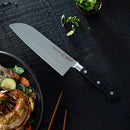 A chef’s knife from the Messermeister Meridian Elite Magnet Block Set - 6 Piece, featuring a black handle, rests on a dark wooden surface beside salad with lobster, chopsticks, and chopped green onions.