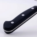 Close-up of the Messermeister Meridian Elite Kullens Vegetable Knife - 7" black handle with three silver rivets, resting on a white surface. The blade is barely visible in the upper right corner.