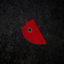 The Messermeister Red Mini Silicone Bowl Scraper, featuring a semicircular shape and a small hole near the straight edge, rests on a dark, textured surface.