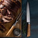 A sliced roast beef rests on a wooden board, with a Messermeister Oliva Elite Kullens Carving Knife - 8" and matching fork with olive wood handles beside it. A bowl of salt and thyme sprigs complete the scene on a dark blue background.