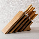 The Messermeister Oliva Elite Next Level Block Set - 11 Piece features German-forged knives with matching olive wood handles, all displayed in a stylish wooden block on a light surface against a patterned wall.
