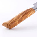 Close-up of the Messermeister Oliva Elite Utility Knife - 6", featuring a smooth, light brown olive wood handle with natural grain patterns and a German stainless steel blade, displayed against a plain white background.