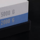 Close-up of the Messermeister Polishing Stone, a dual-sided sharpener with 2000 (blue) and 5000 (white) grit surfaces on a black base, by Messermeister, shown against a dark background.