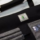 A close-up of the Messermeister Preservation Black Knife Roll - 8 Pocket shows its white PRESERVATION label, green logo, and grey pockets storing chef essentials like a pen and a photo—ideal for sustainable knife storage.