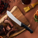 The Messermeister Pro Series Kullens Butcher Knife - 8" with a black handle and high-carbon stainless steel blade sits on a wooden cutting board next to cooked ribs, sliced blood oranges, dried chilies, herbs, sauce, and peppercorns.