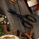 A pair of Messermeister Push Button Take-Apart Multi Shears - 9" rests on a rustic wooden table beside a bourbon bottle, apple slices, cinnamon sticks, dried citrus, fresh mint, and a partially visible pie.