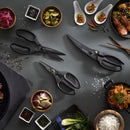 Three pairs of Messermeister Push Button Take-Apart Multi Shears - 9" are surrounded by rice, shrimp, sliced vegetables, kimchi, pickled onions, spices, and sauces on a dark gray surface. These Messermeister shears tackle any kitchen prep with ease.