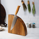 A Messermeister Wood Quarter Round Magnetic Knife Block made from Solomon Walnut sits on a white kitchen countertop, storing knives. Dried herbs hang on the tiled wall, with spice jars nearby for stylish and functional kitchen organization.