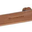 A close-up of the Messermeister Saddle Brown Leather Magnetic Edge-Guard - 6.5", featuring the Messermeister logo embossed, partially covers a knife blade to provide premium protection.