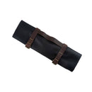 The Messermeister Vintage Leather Black Knife Roll - 7 Pocket, handmade and secured with brown leather straps and brass buckles, offers stylish chef knife storage. Displayed on a white background.