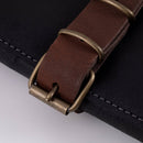 Close-up of a brown leather strap with brass buckles on the Messermeister Vintage Leather Black Knife Roll - 7 Pocket, showing visible edge stitching—an ideal chef knife storage solution by Messermeister.