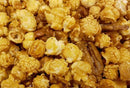 Close-up of Millican Pecan Caramel Pecan Popcorn - 12 oz Bag, featuring popcorn clusters coated in golden caramel glaze with praline pecans for a decadent Millican Pecan gourmet treat.