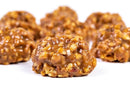 Close-up of several Millican Pecan Texas Chewy Pecan Pralines (individually wrapped) on a white background, with one candy in sharp focus in the foreground. The pralines look satisfyingly chewy and are packed with pecans, capturing the rich flavors characteristic of Millican Pecan confections.
