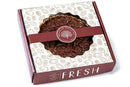 A boxed Millican Pecan Chocolate Pecan Pie – a 9-inch Southern dessert – comes in maroon and white packaging with pecan illustrations, a see-through top, and decorative labels featuring the Millican Pecan brand name. The charming box captures the appeal of this classic pecan pie.