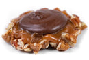 The Millican Pecan Dark Chocolate Caramillicans – Individual Chocolate Caramel Pecan Candy by Millican Pecan features a smooth dark chocolate top, a layer of handcrafted caramel pecans, and chopped pecans around the edges, all presented on a white background.