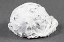 A scoop of white ice cream with small pieces of nuts, inspired by Millican Pecan Divinity Candy—an individually wrapped Southern treat from Millican Pecan—is placed on a plain gray surface.