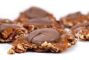 Close-up of Millican Pecan Milk Chocolate Caramillicans—with clusters of pecans topped in rich handmade caramel and a thick layer of smooth milk chocolate—set against a white background. The texture of the crunchy nuts, gooey caramel, and creamy chocolate is clearly visible, making these Chocolate Caramel Pecan Candies ideal for featuring in the Millican Pecan Milk Chocolate Caramillicans Gift Box.
