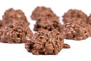 Close-up of a cluster of Millican Pecan Milk Chocolate Pecan Clusters from Millican Pecan, with several more clusters from the gift box softly blurred in the background on a white surface.
