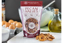 A bag of Millican Pecan Orchard Fresh Raw Pecan Halves - Premium Shelled Texas Pecans sits on a kitchen counter near pecans, eggs, oil, and a glass container, with a baking dish partially visible.