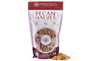 A bag of Millican Pecan Orchard Fresh Raw Pecan Halves - Premium Shelled Texas Pecans stands upright with raw pecan halves visible through a clear window and several pecans scattered in front, nutrition info on the label.
