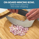 Hands use a curved mincing knife to chop red onion on the NULU Signature Cutting Board by NULU Inc., demonstrating an integrated mincing bowl that keeps food in place for easy rocker chopping. Text above explains the product’s purpose.