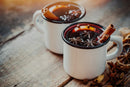 Two white mugs filled with mulled wine, infused with aromatic World Spice Mulling Spice by World Spice and garnished with cinnamon sticks, star anise, and orange slices, sitting on a rustic wooden surface.
