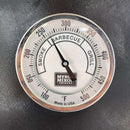A close-up of the Myron Mixon Smokers 5" High Visibility Temperature Gauge displays a temperature near 250°F, with labeled smoke, barbecue, and grill zones. The dark background highlights the Myron Mixon Smokers branding on the dial.