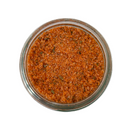 A glass jar of SALTOPIA Infused Sea Salts' Tomato & Italian Herbs Seasoning: MYSTICAL PIZZA, a coarse, reddish-brown blend, viewed from above against a white background.